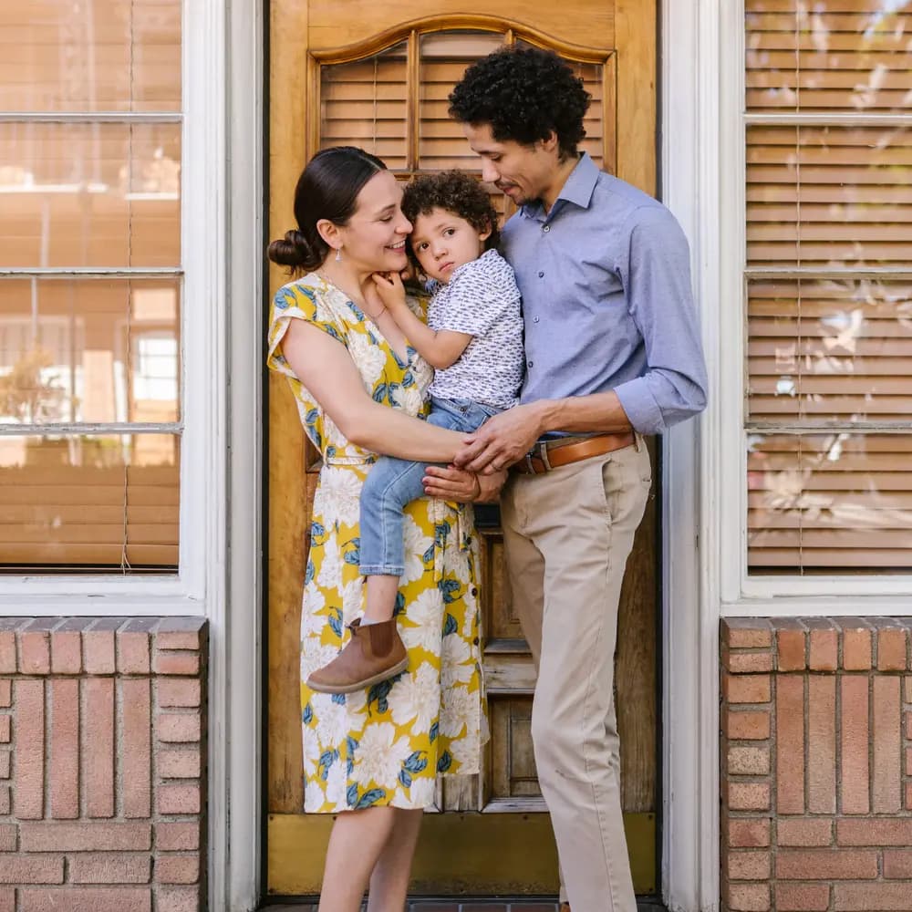 A family of three standing together at the entrance to their home